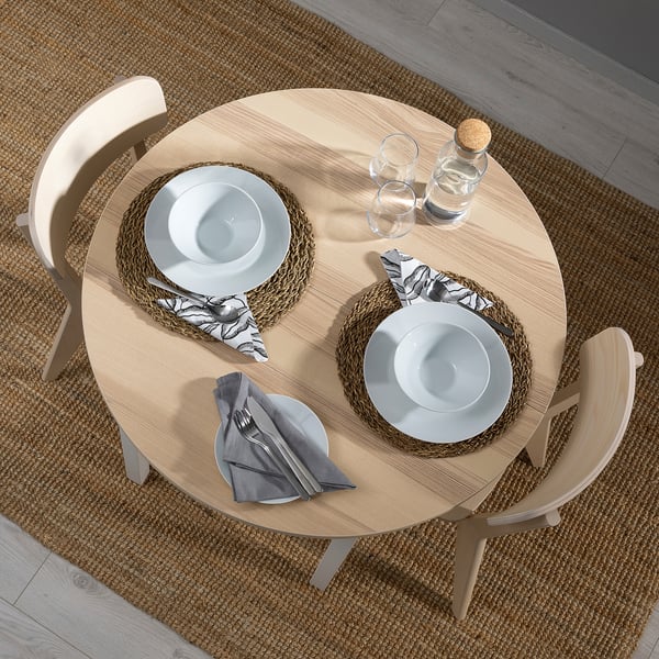 Small round dining table with two light wood chairs, white plates, grey napkins, and patterned napkins.