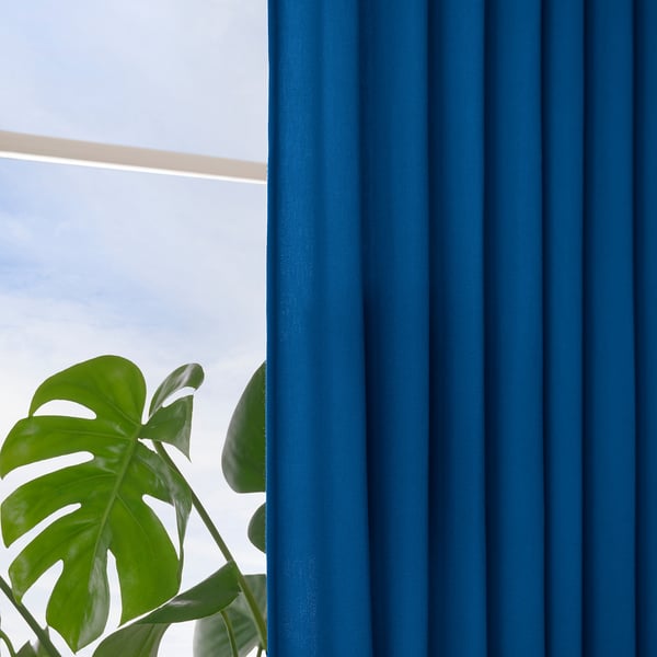 Blue curtains hang by a window, allowing light while offering privacy. A large green leafy plant sits nearby, adding natural decor.