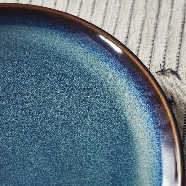 Blue glazed plate with gold rim on striped cloth.