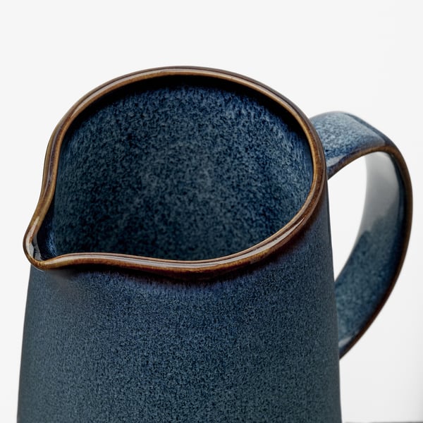 Handcrafted stoneware jug, deep blue with gold trim, sturdy handle, reactive glaze finish.