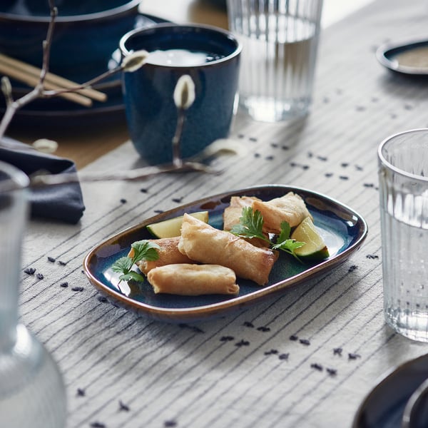 Blue plates, cups, spring rolls, lime wedges. Golden-brown, handcrafted.