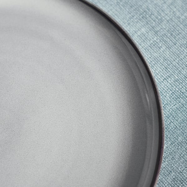 Close-up of a sturdy, textured stoneware plate with a unique, reactive glaze pattern on a light blue background.