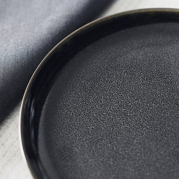 Dark grey glazed side plate, smooth edge, textured surface, placed on folded fabric.
