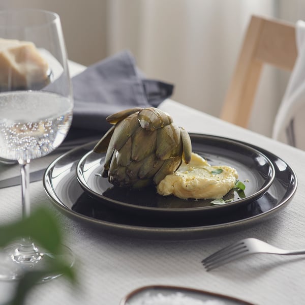 Plate with glazed finish serves artichoke and dipping sauce; glass with sparkly liquid nearby.