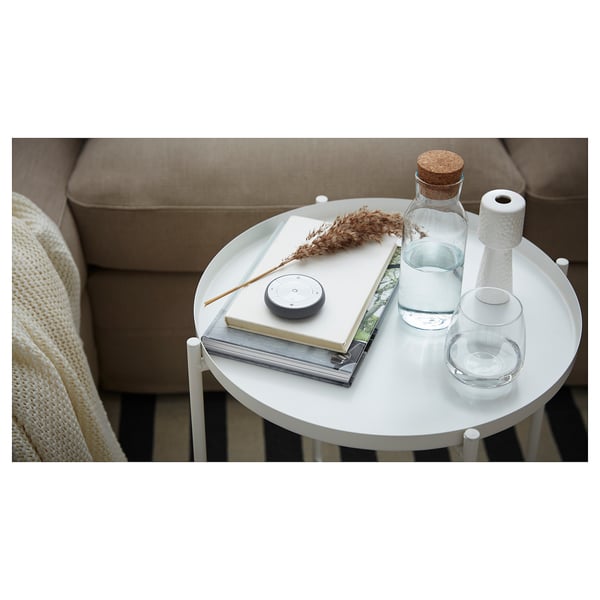 Minimalist round side table with beige sofa, white tray top, books, water bottle, and speaker. Modern and functional design.