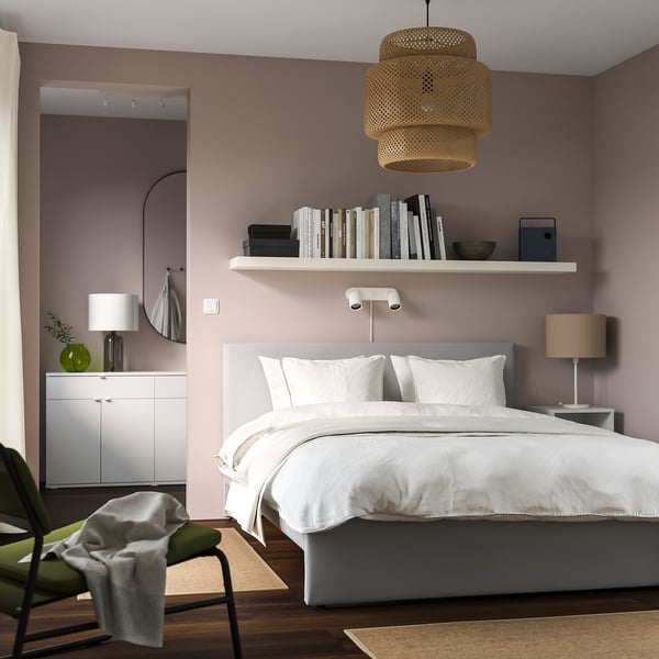Modern bedroom with pink walls, white GLADSTAD bed, grey headboard, shelf of books, bamboo lamp, and small side tables.