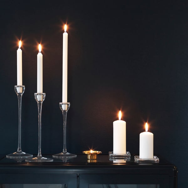 Four lit candles in clear glass holders on dark table; two tall, two short.
