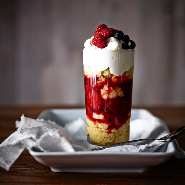 Tall glass dessert cup filled with layers of cake, cream, and berries; perfect for sweet treats.