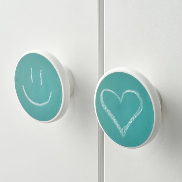 Two teal circular magnets, one with a smiling face, one with a heart, stuck on a white surface.
