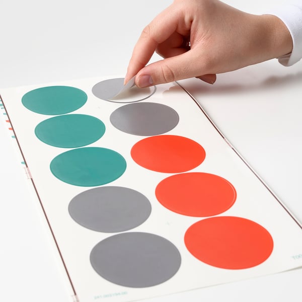 Person organises multicoloured dot stickers on clear sheet; useful for labelling and tracking items.