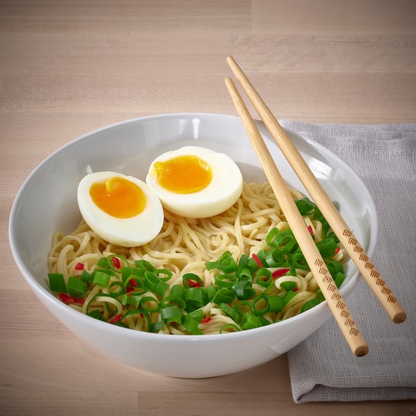 A bowl of noodles with chopped scallions and a halved boiled egg. The bowl is white and accompanied by wooden chopsticks.