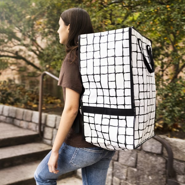 A person carrying a GÖRSNYGG backpack in black and white, larger than typical backpacks, designed for carrying or moving large loads.