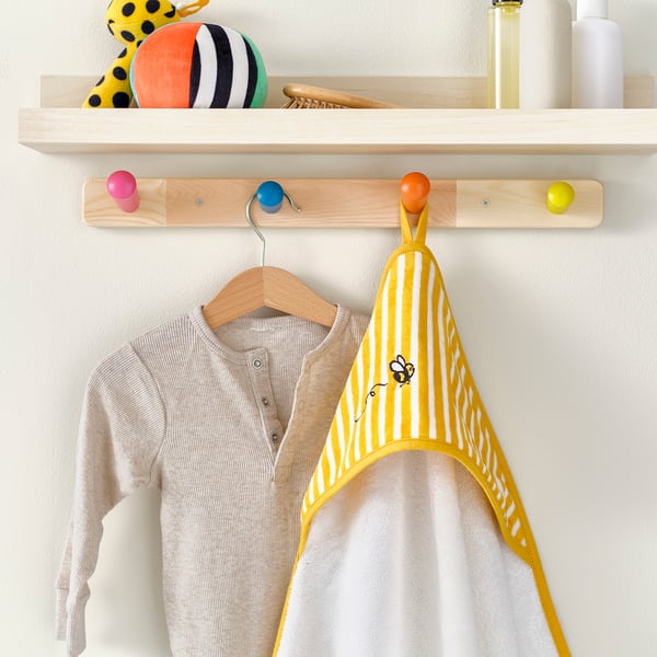 Childrens towel with bee design hangs from hook; wooden shelf with toys above.