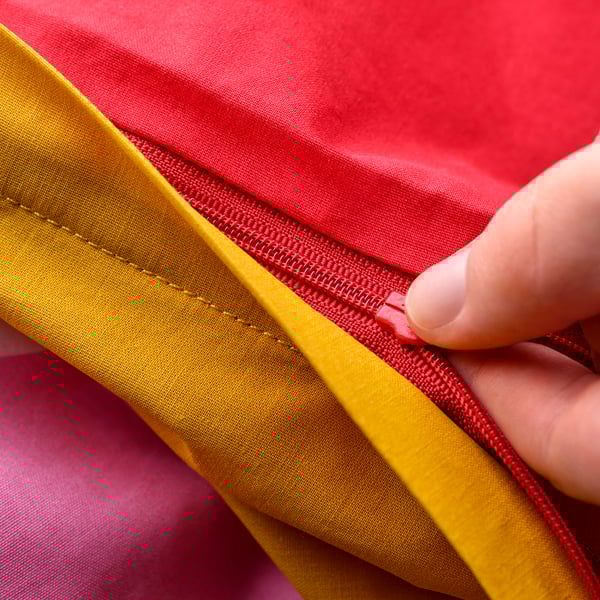 A hand zips a colourful baby duvet, showing its safety feature.