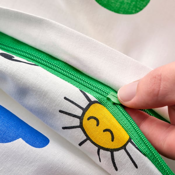 A hand opening a green-zippered duvet cover featuring a yellow sun and blue cloud.