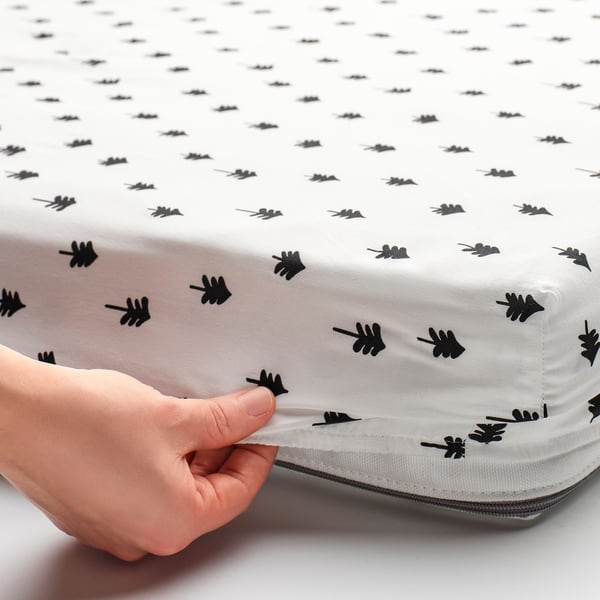 A hand secures a fitted sheet with tree patterns onto a mattress, keeping it safe and comfortable for a child.