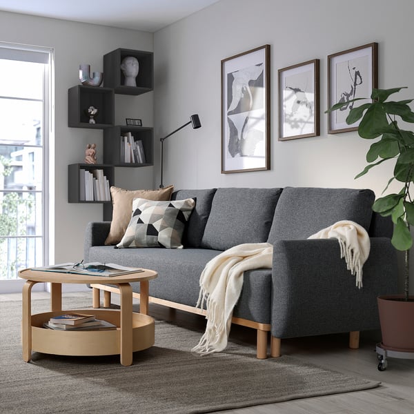Modern living room with GRUNNARP sofa-bed, pillows, throw, coffee table, plant, bookshelf, rug.