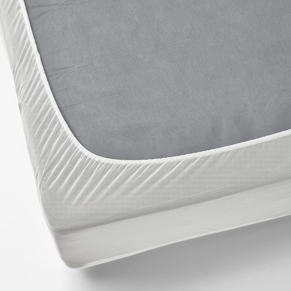 A corner of a grey, waterproof mattress protector with a white, textured elastic edge, designed to fit securely and protect mattresses from stains.
