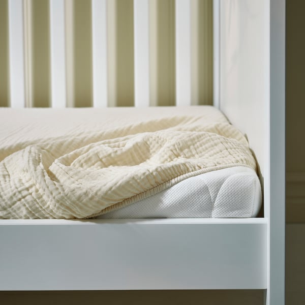 Bed with white GULDVÄVARE cotton muslin duvet, pillow, and fitted sheet, ensuring babys comfort and safety.