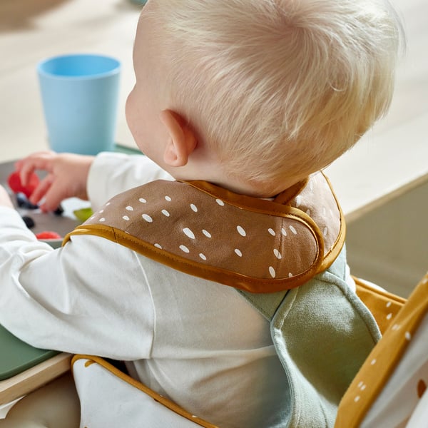 Child wearing dotted bib for feeding, waterproof front, soft cotton back.