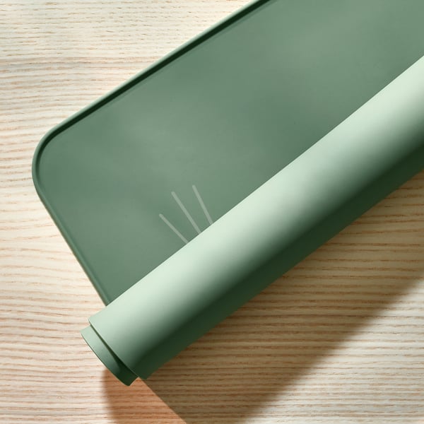 Green silicone place mat with cat ears on wooden table. Protects surfaces from spills and scratches.