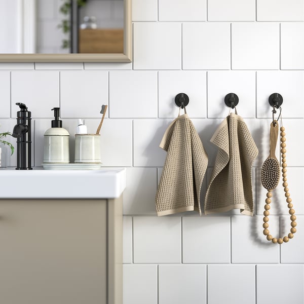 Bathroom with white tiled wall, light brown towels, black hooks, black dispensers, toothbrush, wooden beaded decoration.