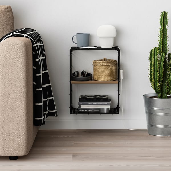 Modern wall-mounted shelf holding a lamp, mug, basket, and books next to a cosy couch with a blanket.