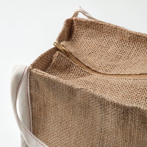 Close-up of a durable, woven jute bag with cotton handles, featuring a gold zip pull.
