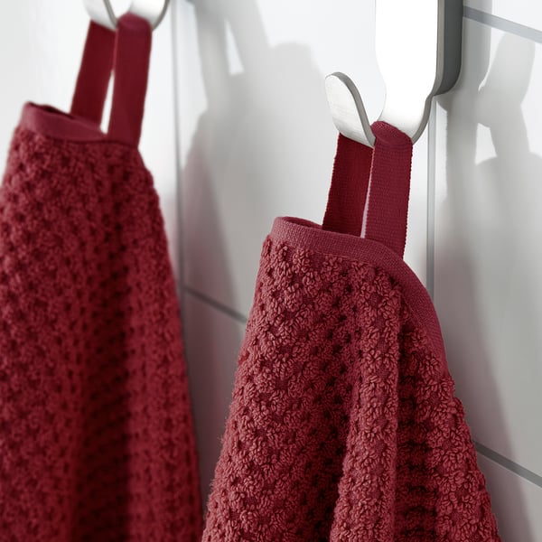 Two maroon towels with red straps hang from metal hooks attached to a white tiled wall.