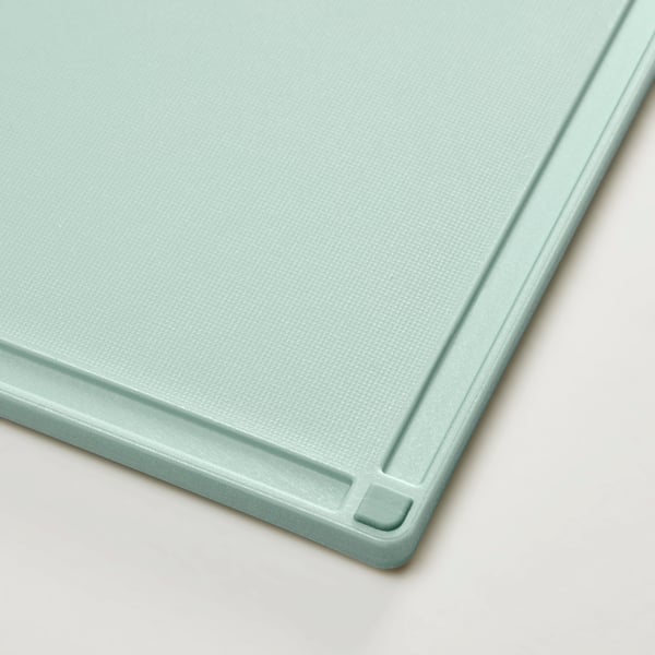 A close-up of a green plastic chopping board, smooth surface, non-slip edges, milled juice groove.
