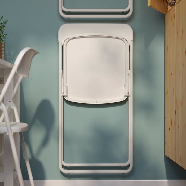 A folded white GUNDE chair mounted on a light blue wall, space-saving design.