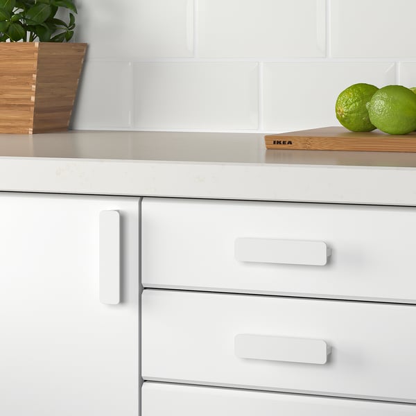 Modern kitchen cabinets with white handles, smoothly finished. Two green fruits on a wooden cutting board, complementing the clean, minimalist style.