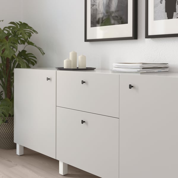 White cabinet with black HACKÅS handles; holds candles, books, and plant.