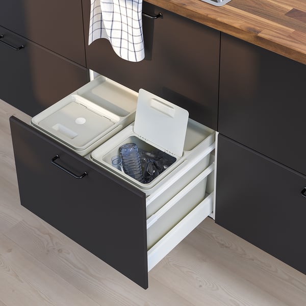 Modern kitchen drawer with pull-out waste sorting bins. Black drawer, two white bins, lids, and black handles.