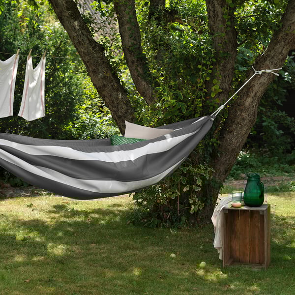 Black & white hammock between green trees. Wooden crate with jug and lemon. Clothesline with towels.