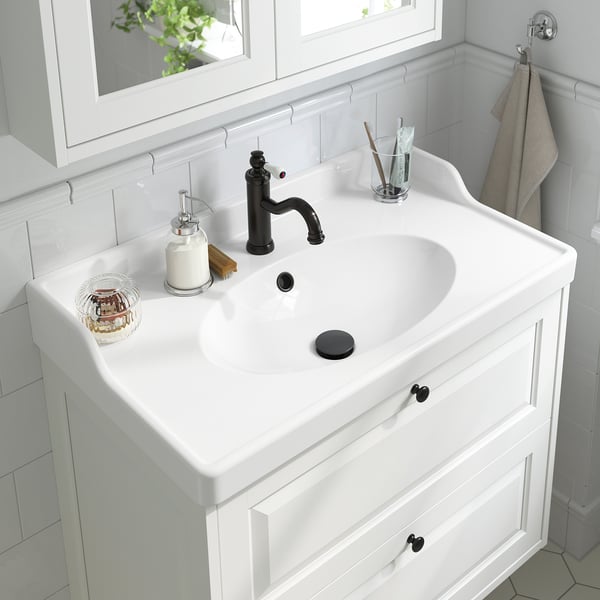 White bathroom sink with black tap and lever, aerator, soap dispenser, toothbrush holder.
