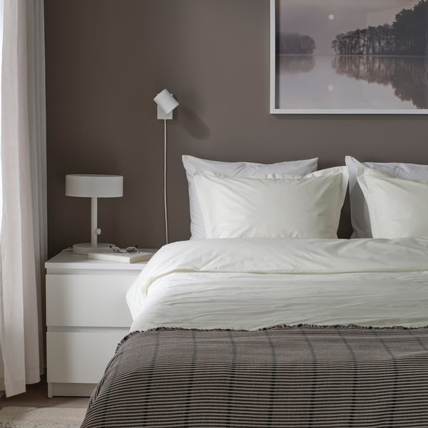 Made bed with white HAMPFLOCKEL duvet, crisp cotton weave. Grey wall, small white bedside table with lamp.