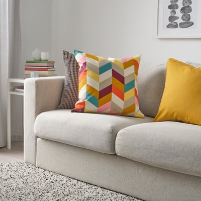 Chevron cushion & yellow pillow on gray couch, books & vase on white table.