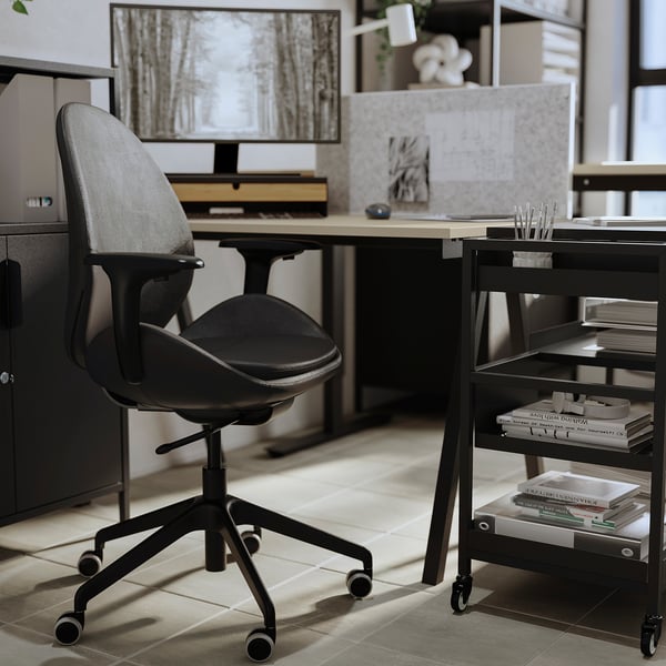 Modern office setup with sleek black HATTEFJÄLL chair, wooden desk, computer monitor, and mobile shelves.