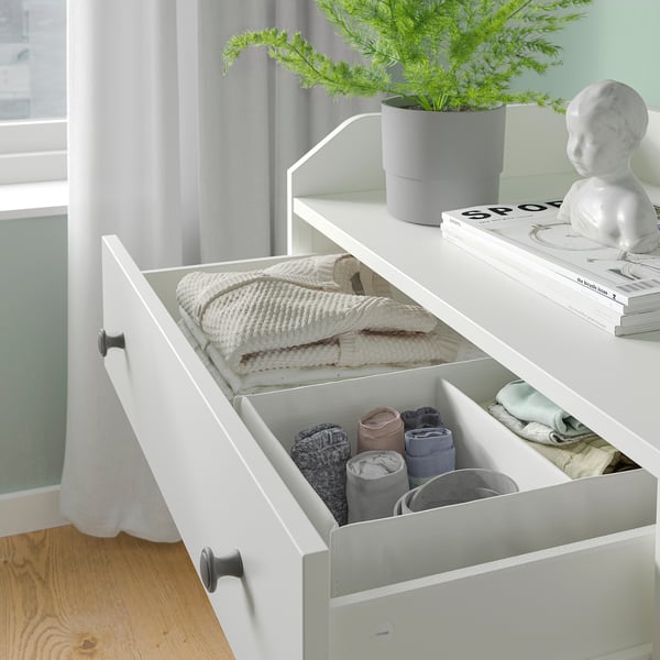 White HAUGA bedroom storage set with socks and sweaters organised in drawers. Plant and decor on top.