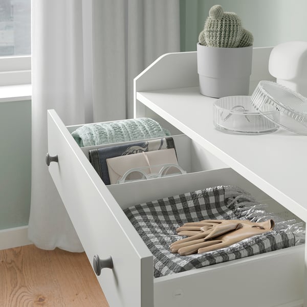 Open white HAUGA drawer reveals neatly folded clothes and gloves on a checked cloth. A potted cactus sits atop.