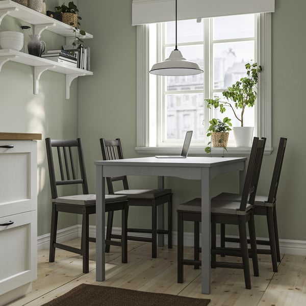 Modern kitchen with grey HAUGA table, four stefan chairs, plant, and laptop. Clean lines, white accents, and large window.
