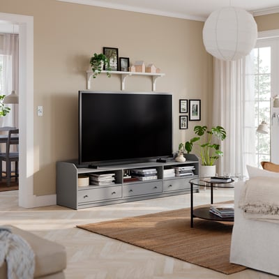 Grey HAUGA tv stand with wide-screen tv, three drawers, coffee table, plants, beige sofa.