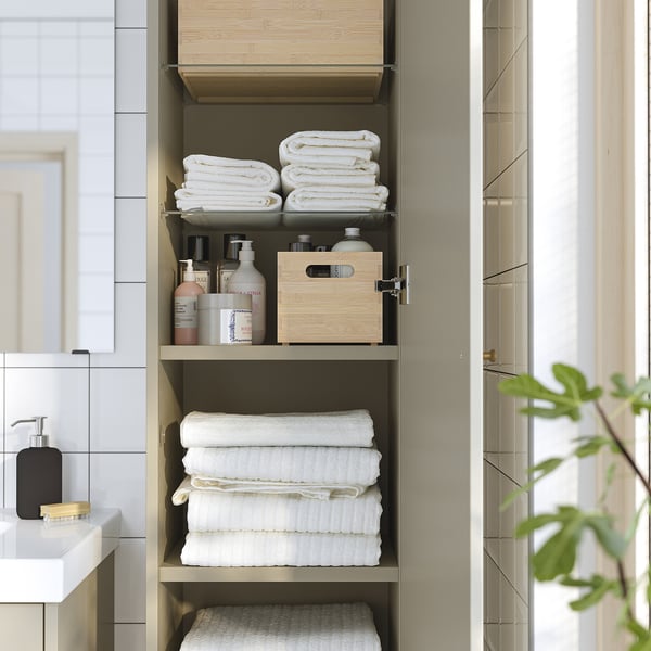 Tall bathroom cabinet with three shelves. Top and bottom hold folded white towels. Middle shelf stores toiletries and a wooden box.