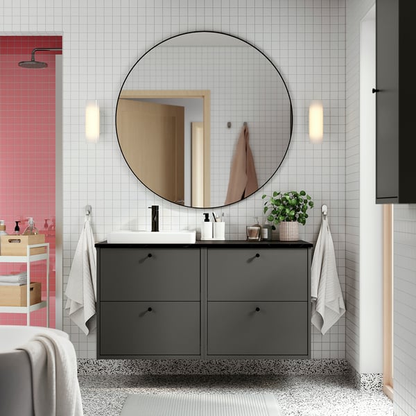 Modern grey bathroom cabinet under large round mirror, with towels and toiletries.