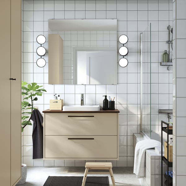 Modern beige bathroom vanity with sleek design, round mirror, plants, and minimalist decor.