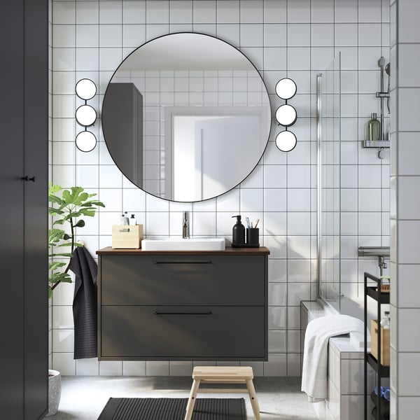 Modern bathroom with dark grey vanity, mirror, lights, stool, and glass shower.