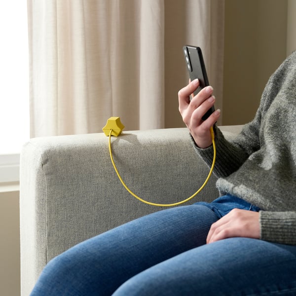 Person on couch using phone, HAVSKÅL cable organiser, casual attire, curtains behind.