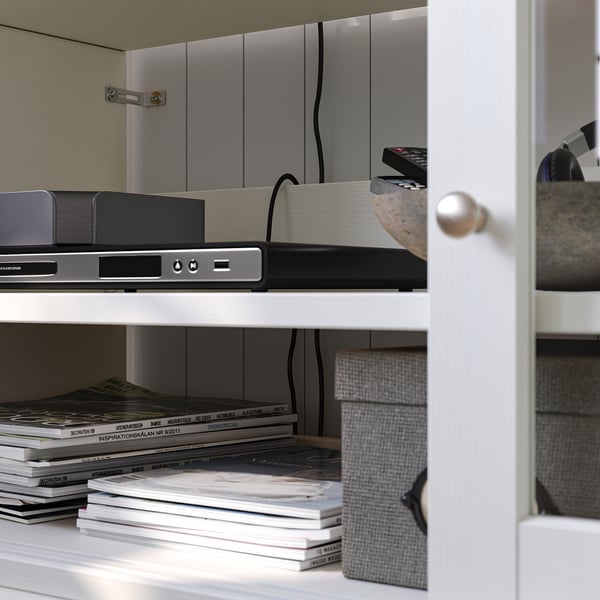 White wooden shelf with electronics, remotes, books, and boxes. Neatly organised with a minimalist design.