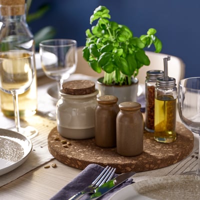 Dark brown cork trivet holds jars, herbs & glasses on dining table.